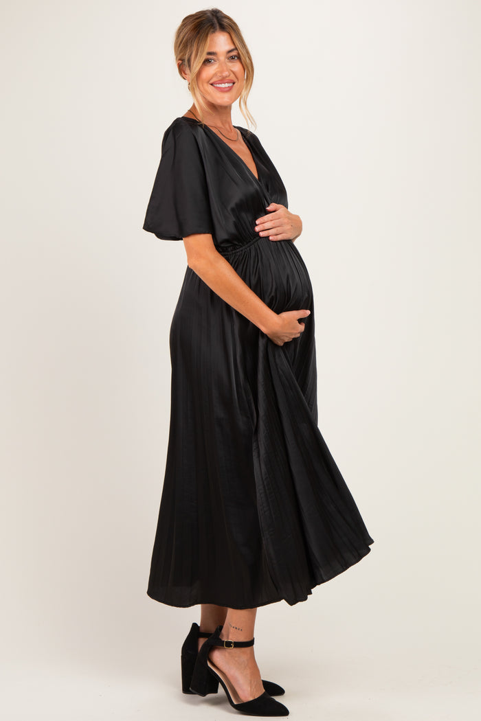 woman wearing a black satin maternity dress with short sleeves and a tied waist, holding her baby bump