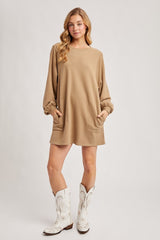 woman wearing a tan long sleeve oversized dress with pockets and white cowboy boots