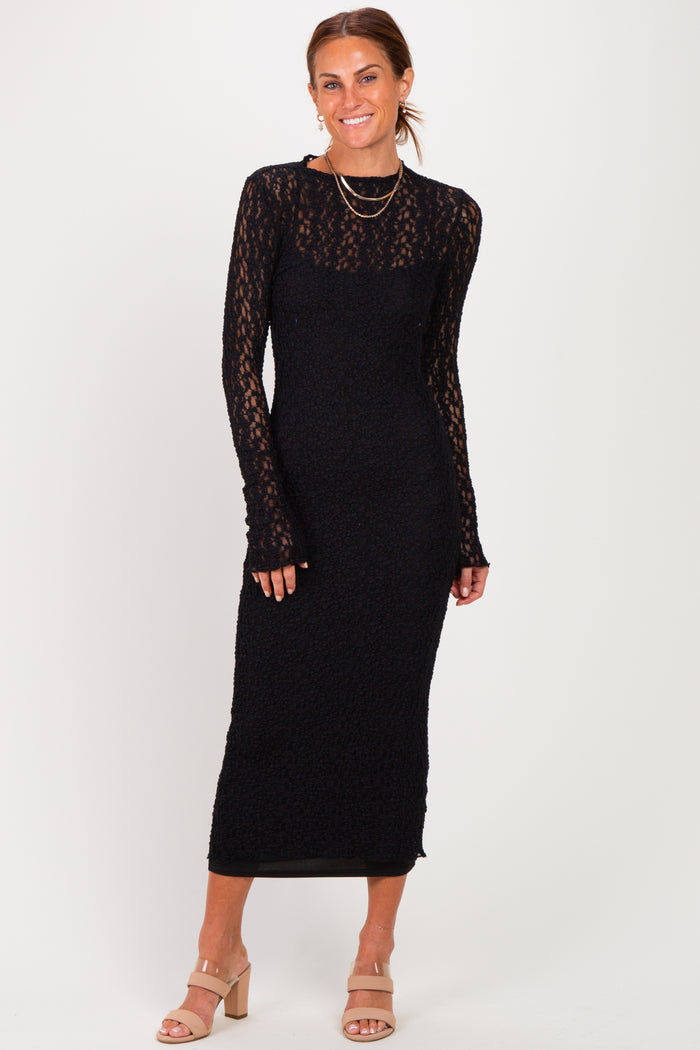 woman wearing a long sleeve black fitted dress with lace details and a midi length, standing and smiling