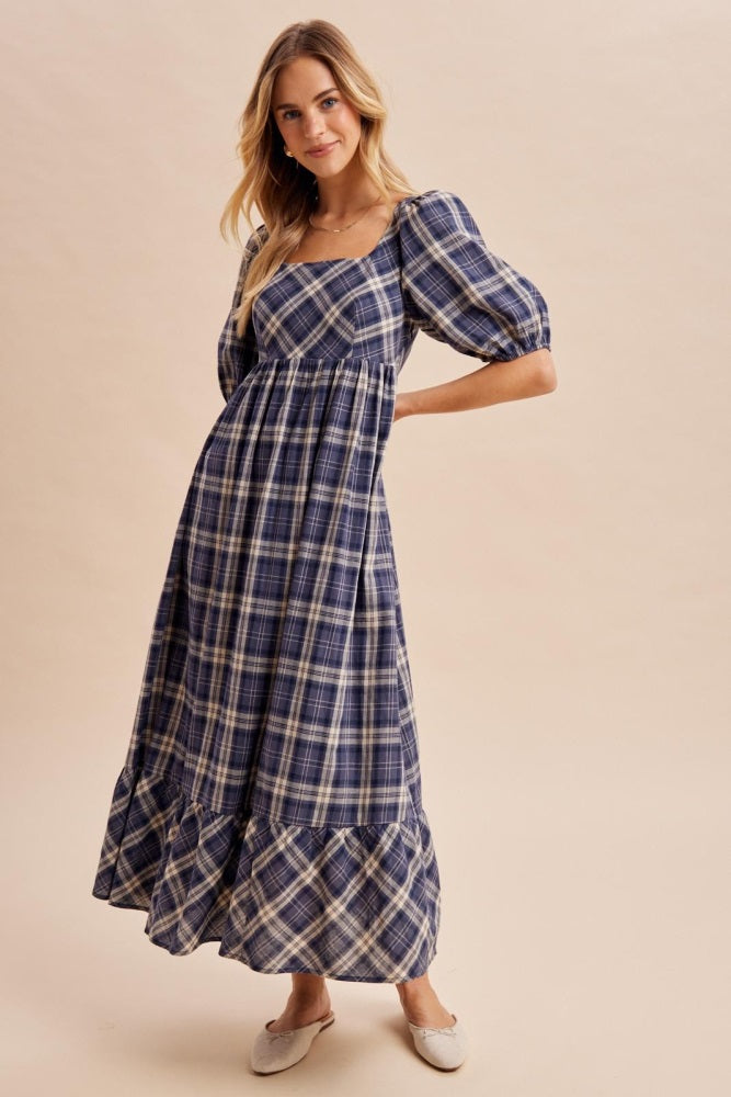 woman wearing a navy plaid maxi dress with puff sleeves and a ruffled hem, standing in a relaxed pose
