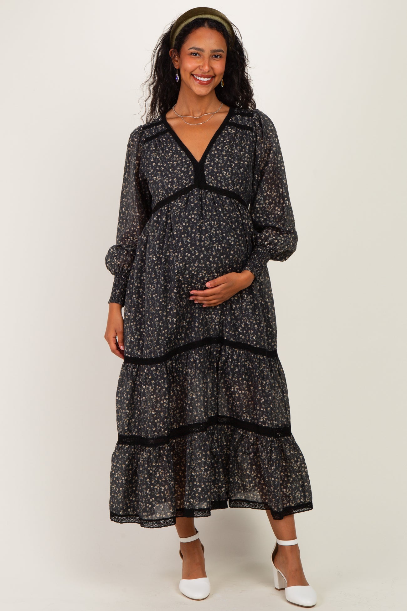 woman wearing a black floral maternity maxi dress with puff sleeves and a baby bump, smiling at the camera