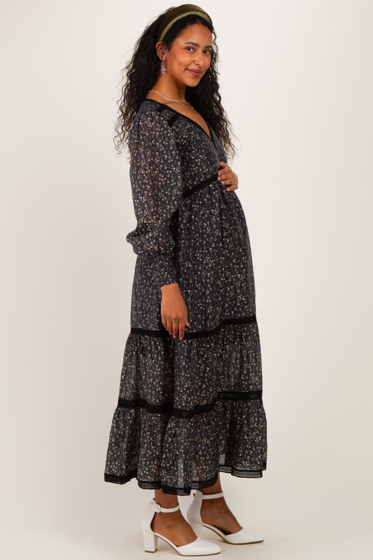 woman wearing a black floral maternity dress with long sleeves and tiered design, showcasing her baby bump