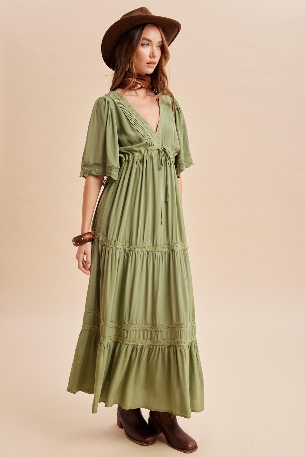 woman wearing a long olive green bohemian maxi dress with short flutter sleeves and a cinched waist, paired with a brown hat