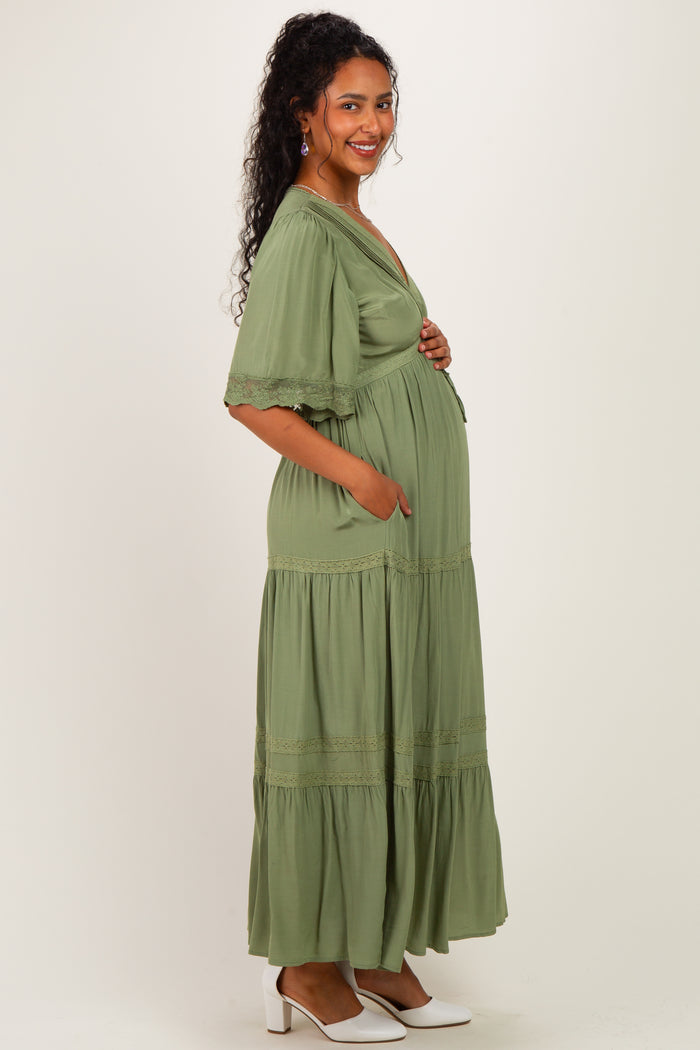 woman wearing a sage green maternity maxi dress with flutter sleeves and pockets, showing her baby bump