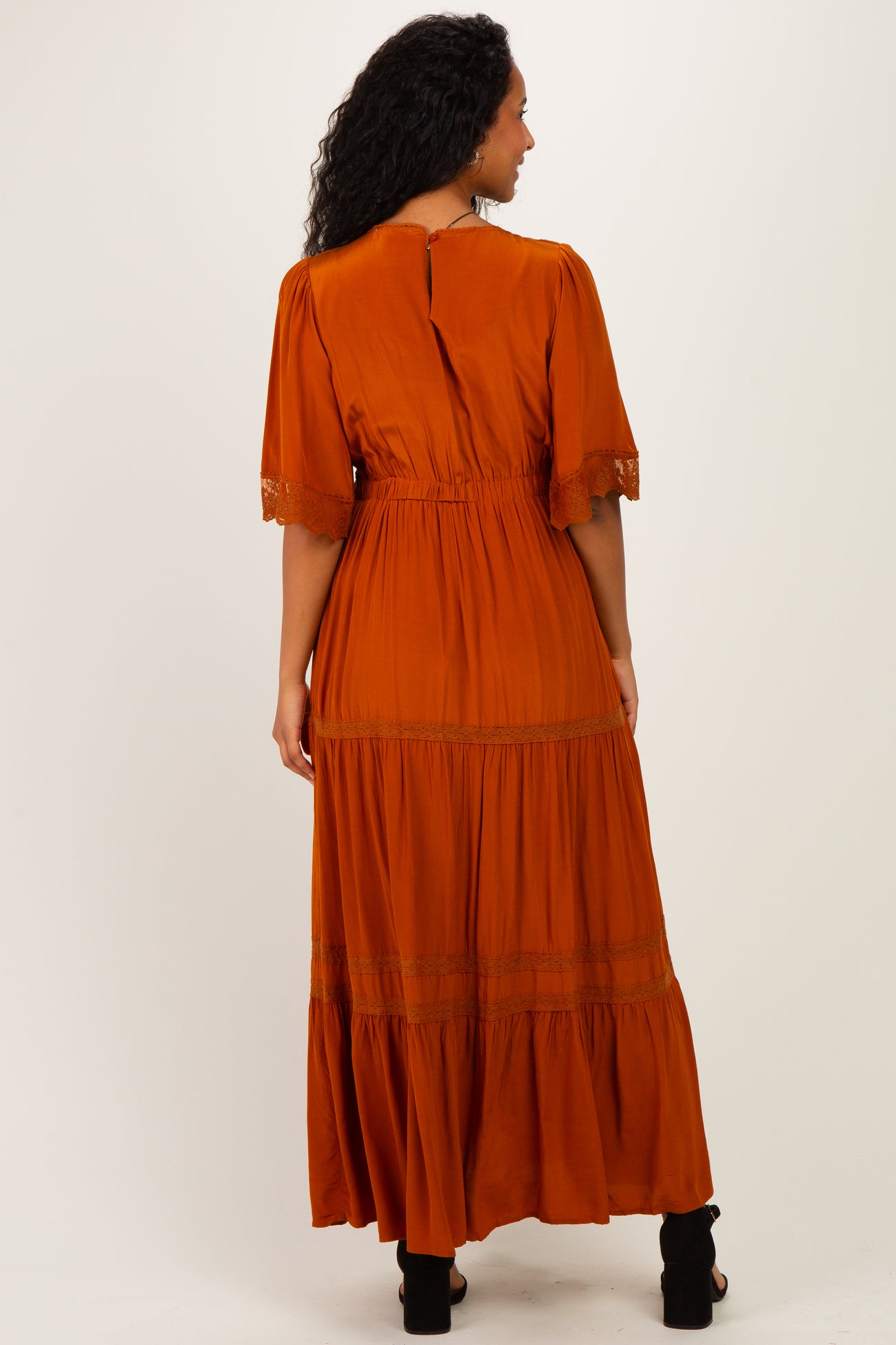 woman wearing a rust orange maternity maxi dress with flutter sleeves and tiered ruffles, showing her baby bump