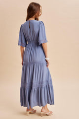 woman wearing a blue maxi dress with short puff sleeves and tiered design, shown from the back