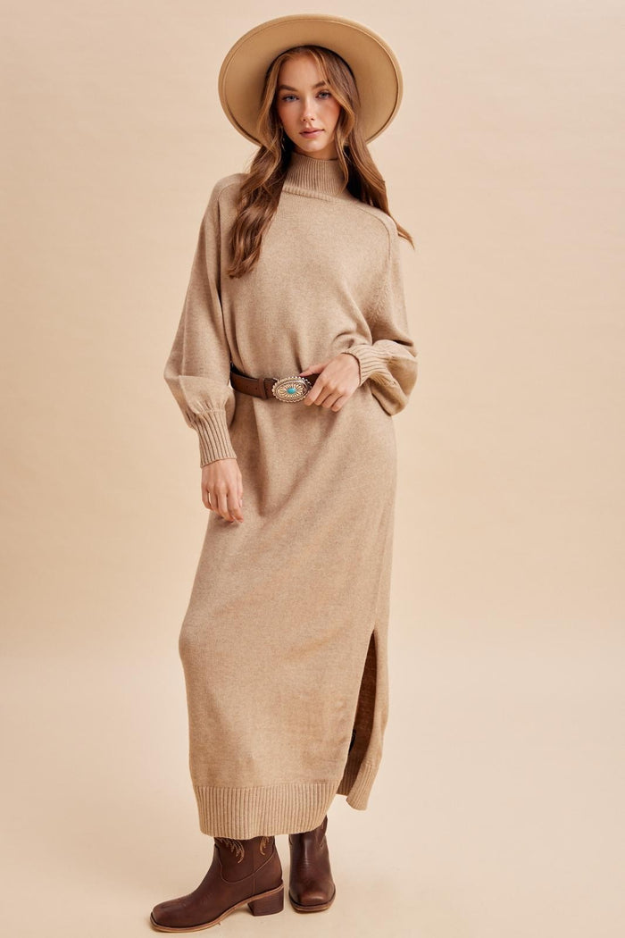 woman wearing a beige long sleeve turtleneck sweater dress with side slits and a wide-brimmed hat, paired with brown boots