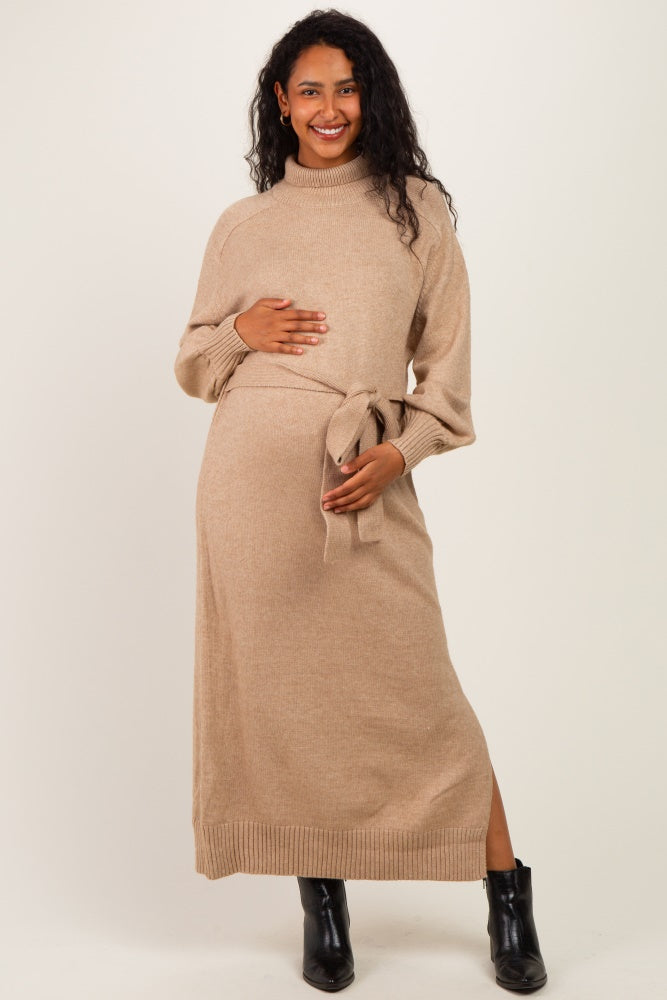 woman wearing a tan maternity sweater dress with a tie waist and long sleeves, showing her baby bump
