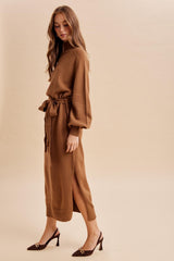 woman wearing a brown long sleeve knit dress with a tie waist and side slits, paired with elegant heels
