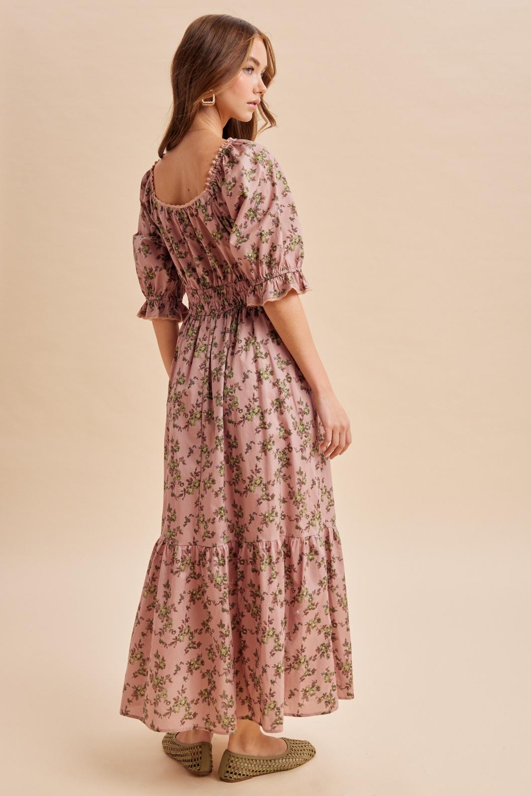 woman wearing a pink floral maxi dress with puff sleeves and a tiered skirt, standing with her back to the camera