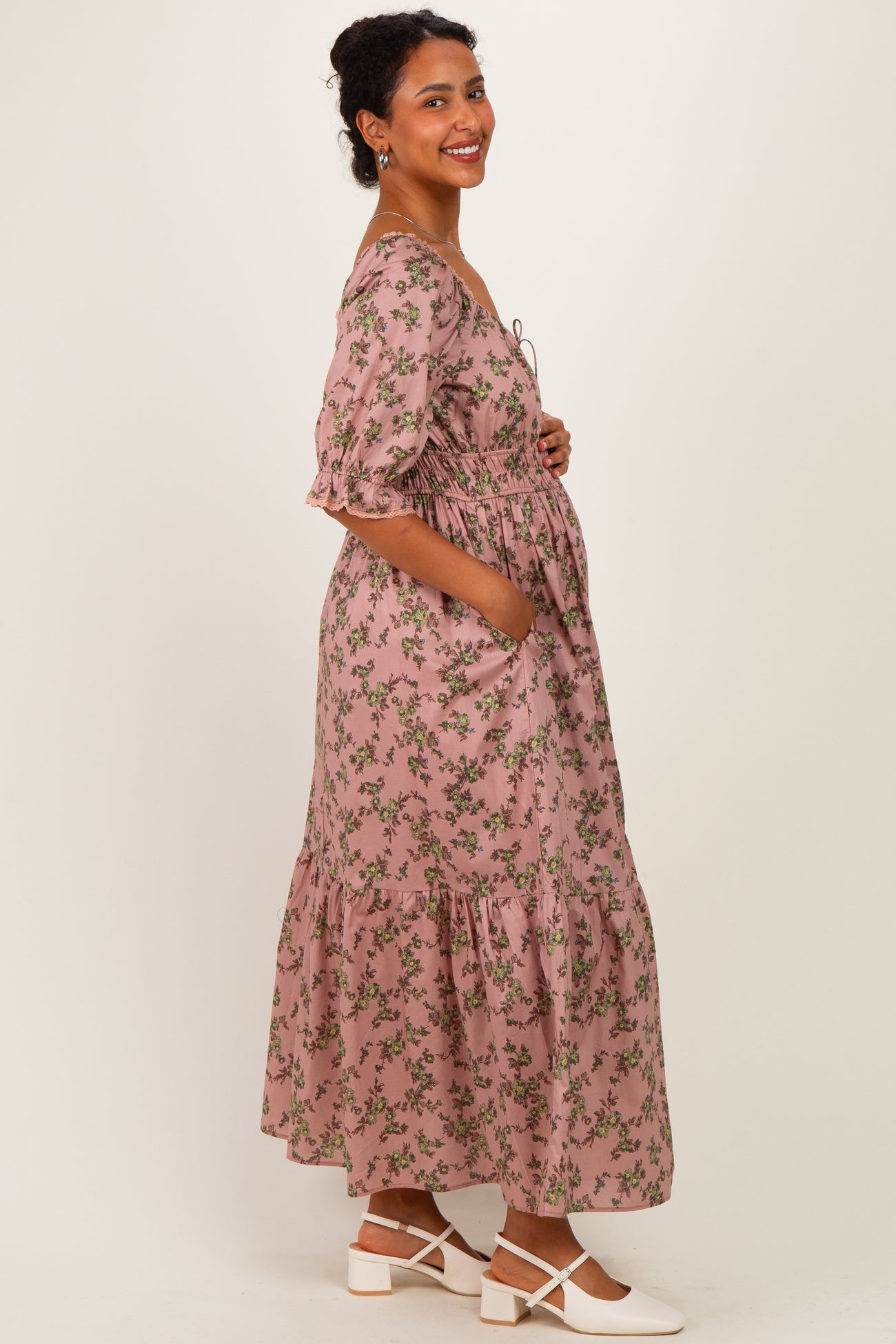 woman wearing a floral pink maternity dress with a tiered skirt and pockets, showing her baby bump