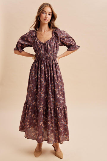 woman wearing a brown floral maxi dress with puff sleeves and a smocked waist, styled with neutral heels