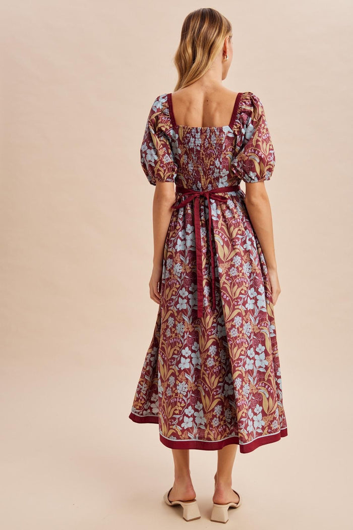woman wearing a floral patterned maxi dress with puff sleeves and a tie waist, seen from the back