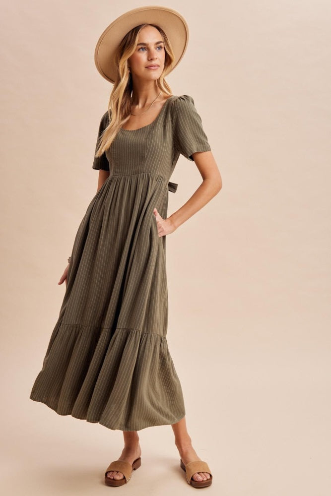 woman wearing an olive green tiered maxi dress with short sleeves and pockets, styled with a wide-brim hat and sandals
