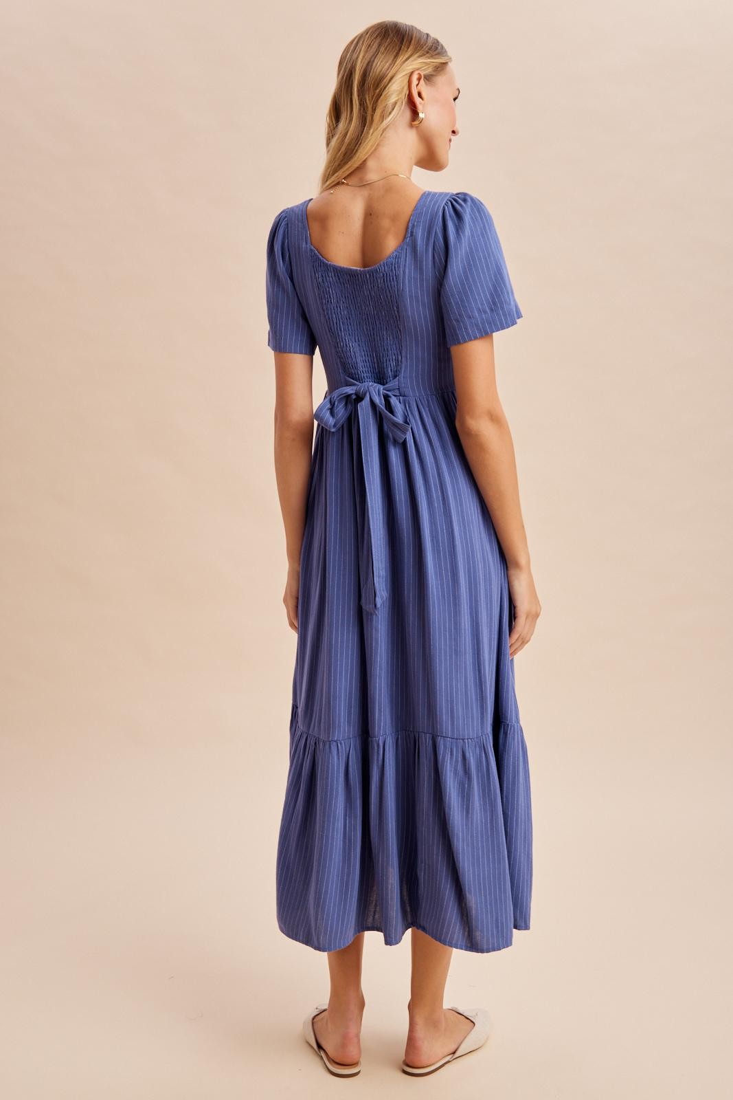woman wearing a light blue short sleeve maxi dress with a smocked bodice and a tie detail at the back