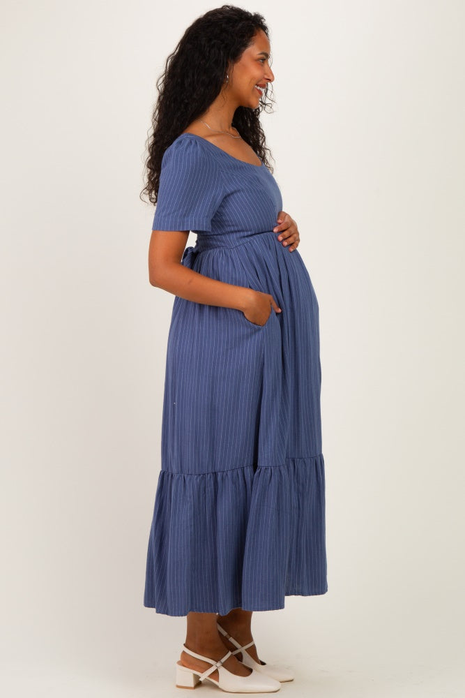 woman wearing a blue striped maternity dress with short sleeves, a belted waist, and a flowy tiered skirt, showing her baby bump