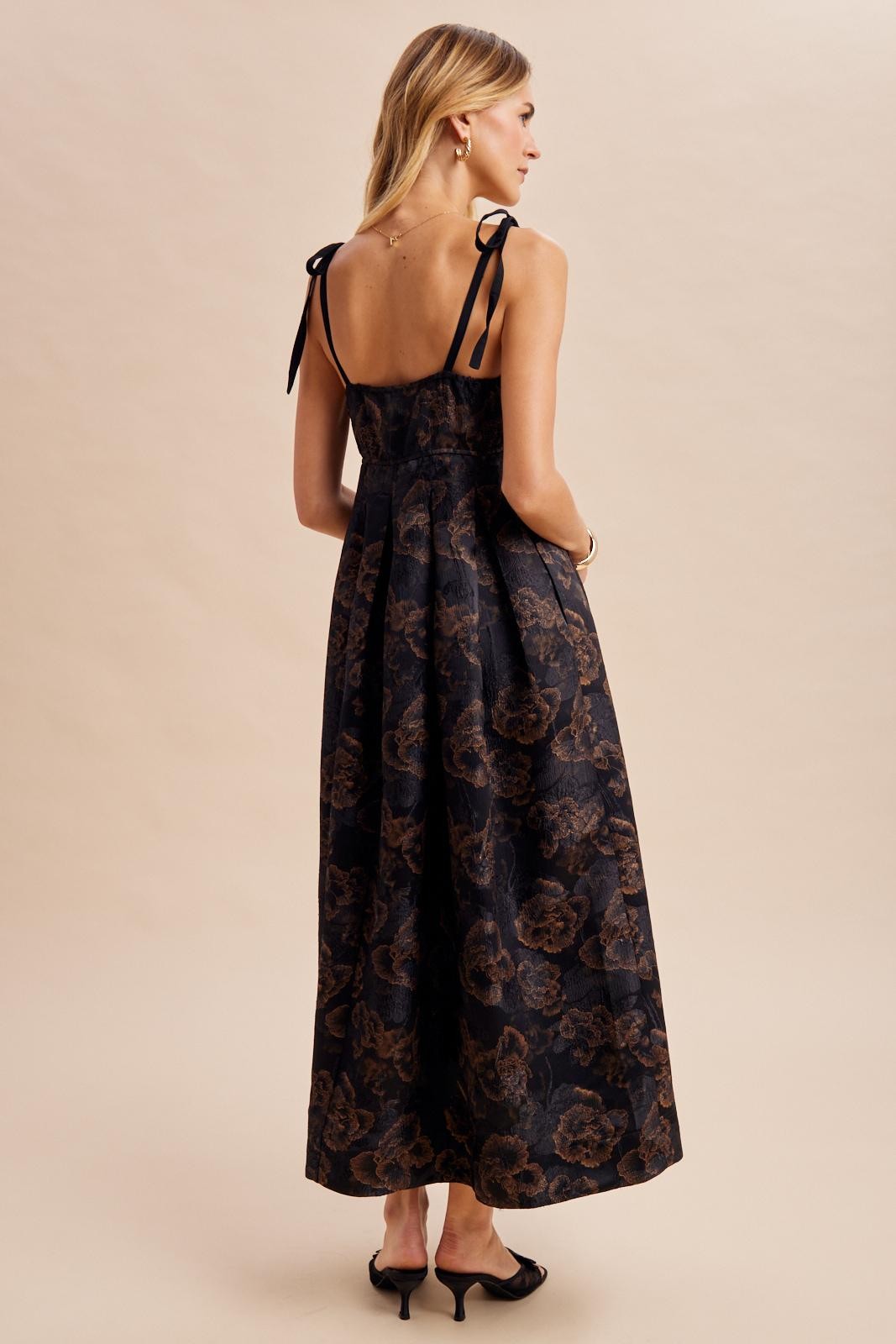 woman wearing a black floral maxi dress with satin straps and pleated detailing, showing the back view