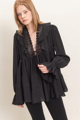 woman wearing a black long sleeve blouse with ruffled neckline and bell sleeves paired with black leggings