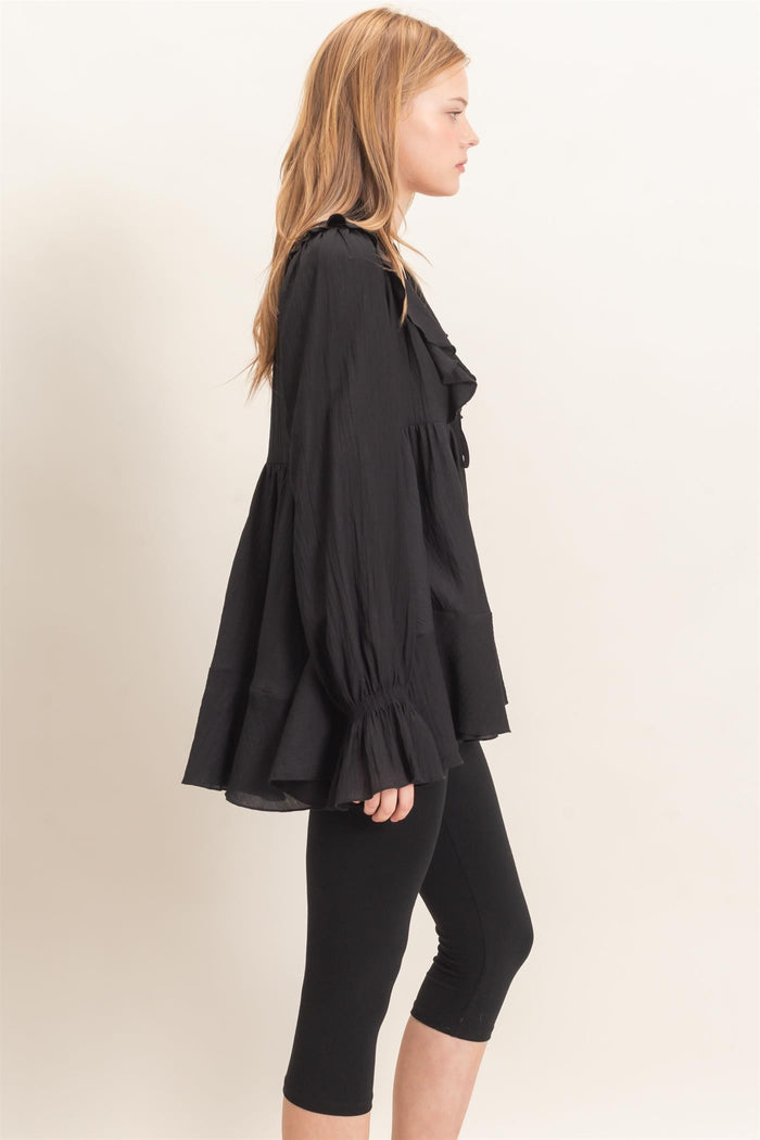 woman wearing a black pleated blouse with ruffled details and bell sleeves paired with black leggings