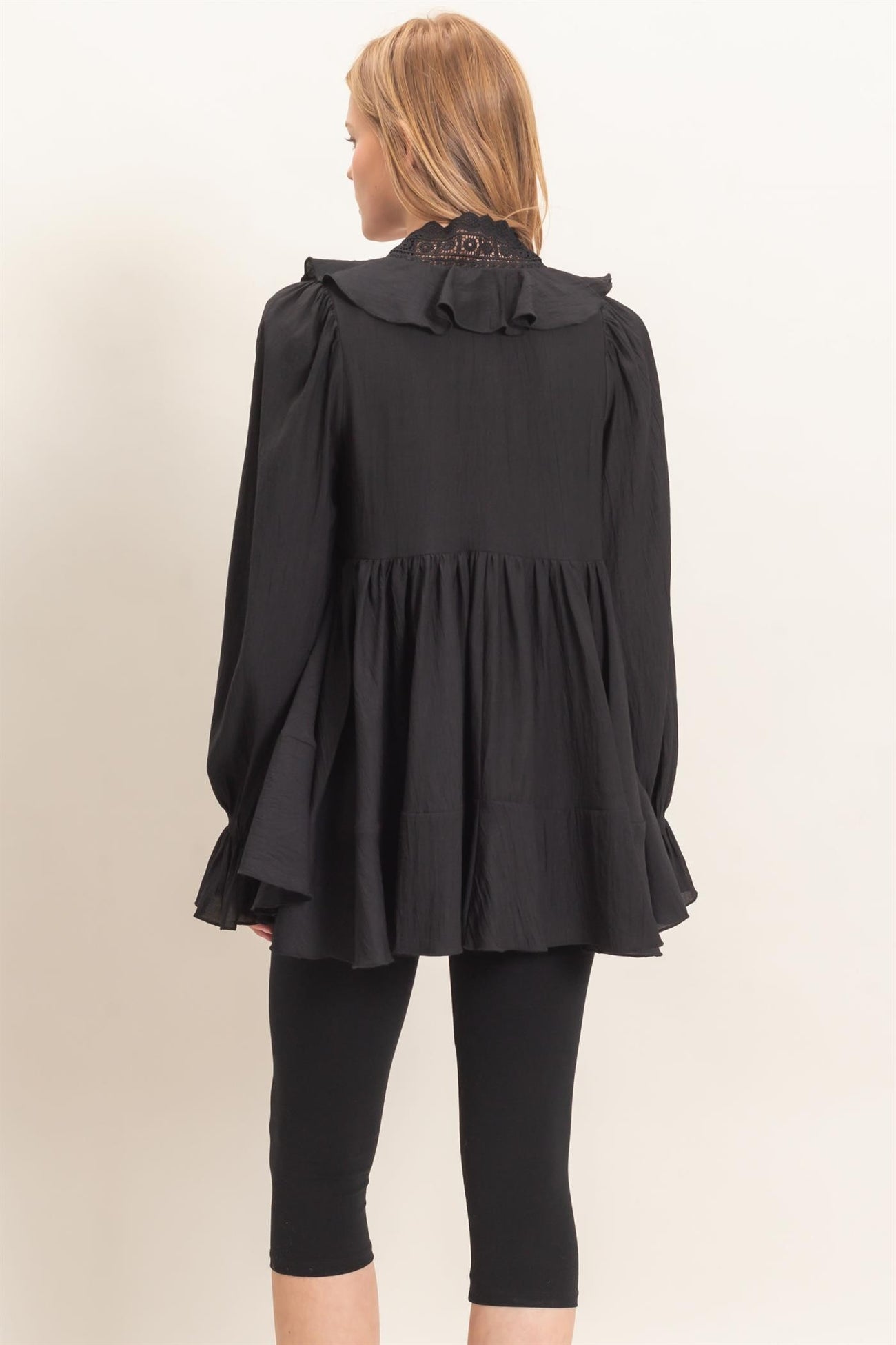 woman wearing a black long sleeve blouse with a frilled collar and peplum hem paired with black leggings