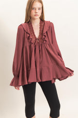 woman wearing a maroon ruffled blouse with a tie at the neckline and long sleeves, paired with black leggings