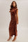 woman wearing a brown velvet maxi dress with ruching details and a high neck, styled with strappy heels