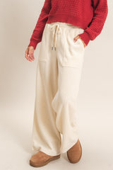 woman wearing cream wide-leg lounge pants with pockets and a red textured sweater
