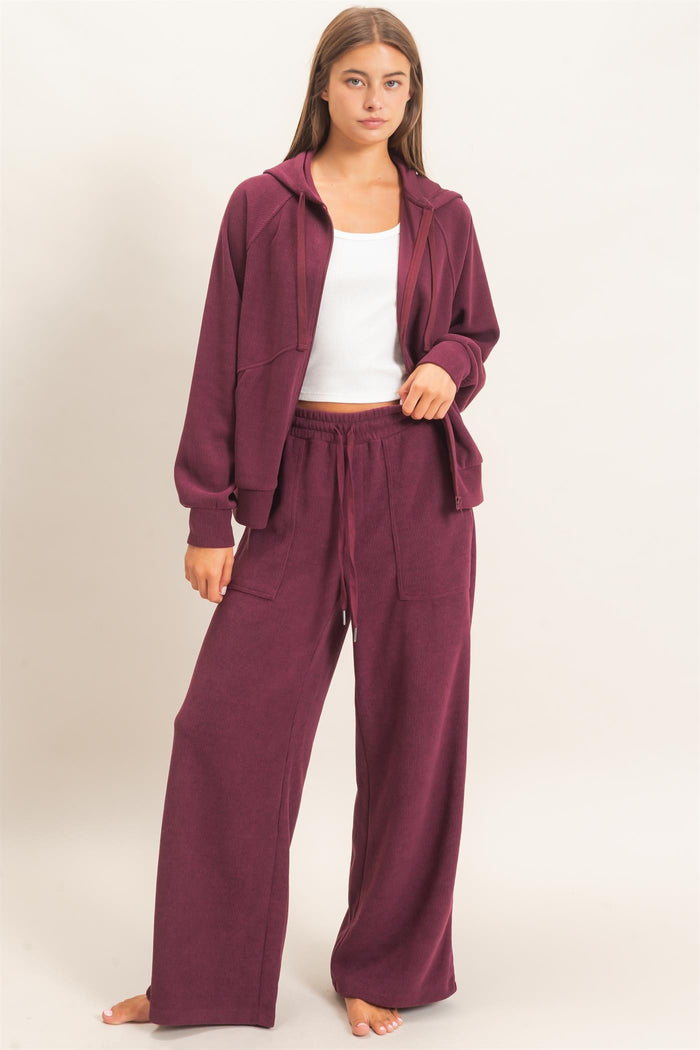 woman wearing a burgundy ribbed loungewear set consisting of a zip-up hoodie and wide-leg pants