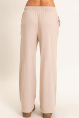 woman wearing light beige wide-leg pants with an elastic waistband and side pockets, viewed from the back