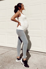 woman wearing a white maternity tank top and light blue maternity leggings, showcasing a visible baby bump