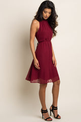 woman wearing a sleeveless burgundy chiffon halter dress with a waist tie and black strappy heels