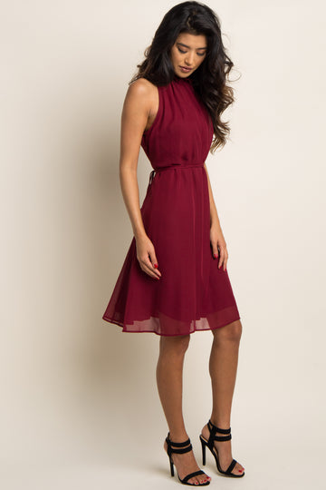 woman wearing a sleeveless burgundy chiffon halter dress with a waist tie and black strappy heels