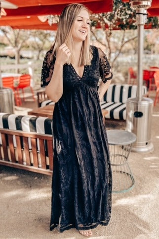 woman wearing a black lace maxi dress with short sleeves and a v-neckline, standing outdoors
