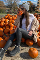 woman sitting among pumpkins wearing a white t-shirt, black jeans, and a cozy beige cardigan, drinking from a mug
