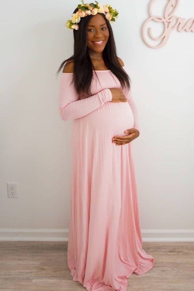 woman wearing a light pink off-the-shoulder maternity maxi dress and holding her baby bump