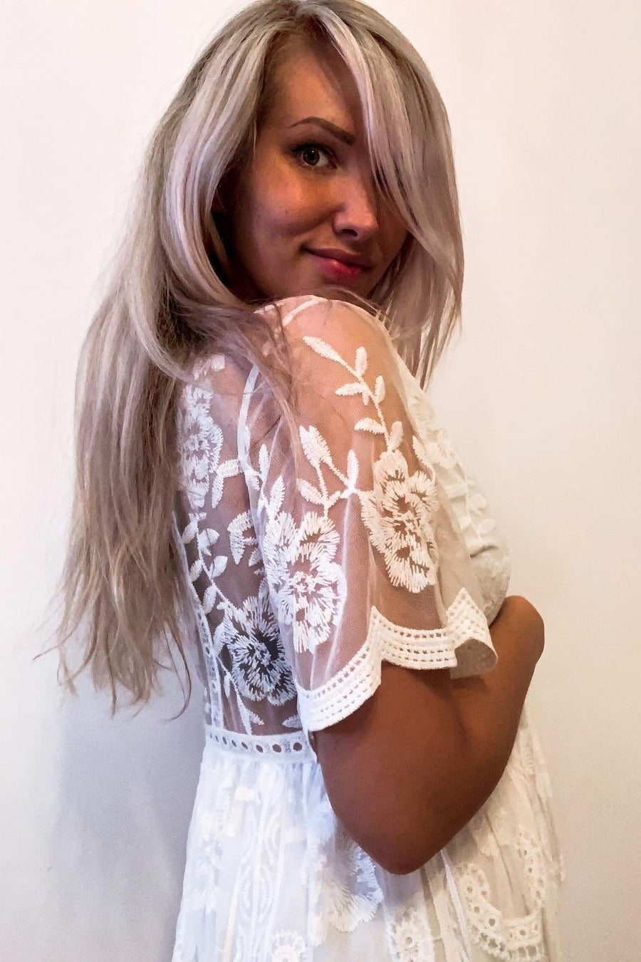 woman wearing a white maternity dress with floral lace details and a visible baby bump