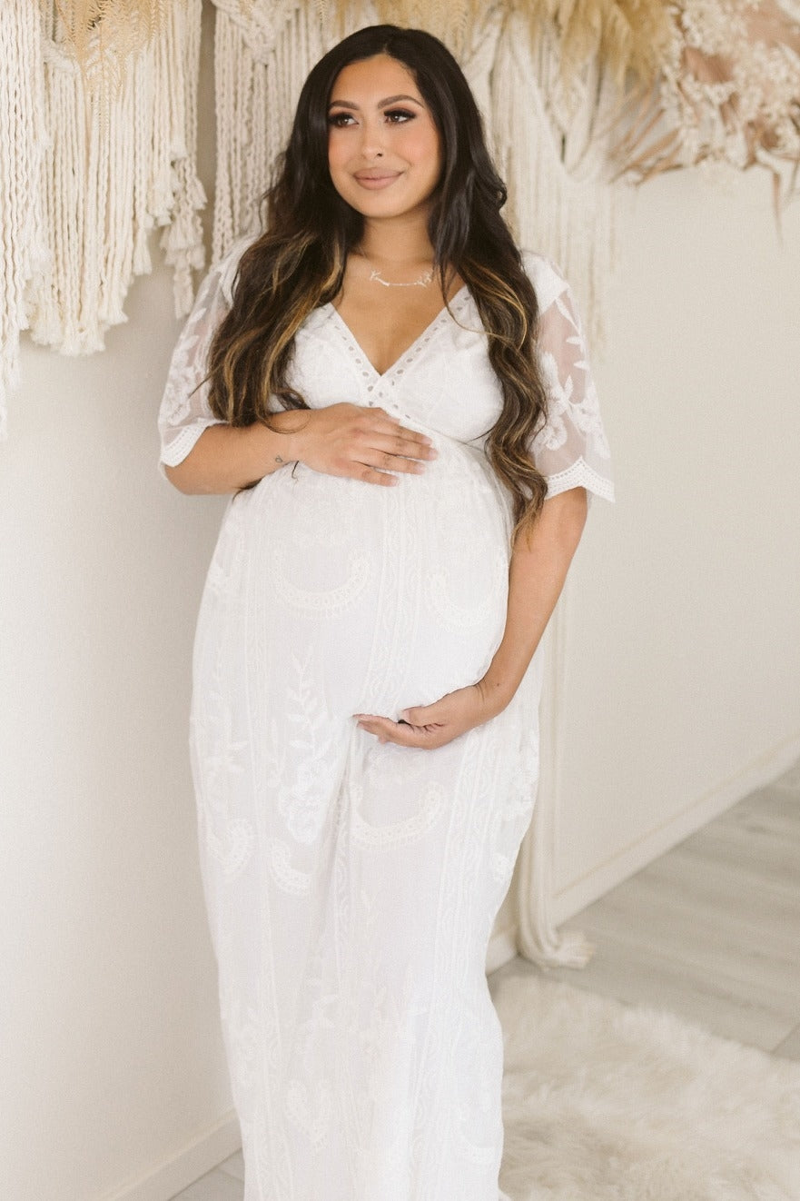 woman wearing a white lace maternity gown and holding her baby bump