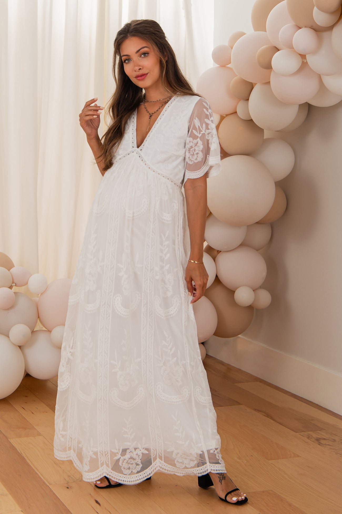 woman wearing a white floral embroidered maternity maxi dress with short sleeves and a v-neckline, showcasing her baby bump
