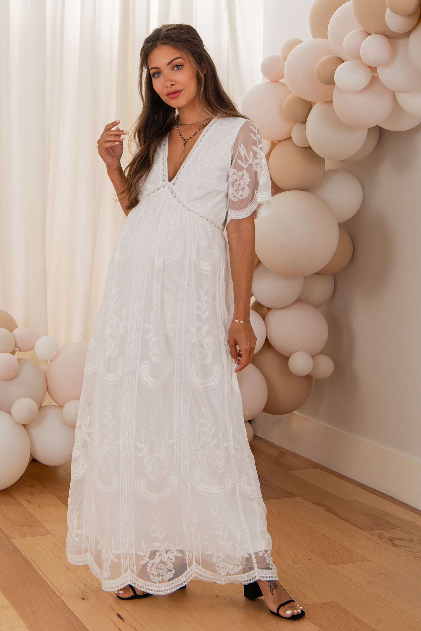 woman wearing a white floral embroidered maternity maxi dress with short sleeves and a v-neckline, showcasing her baby bump