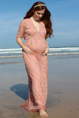 woman wearing a soft pink lace maternity dress with short sleeves and a v-neck, showing her baby bump on the beach