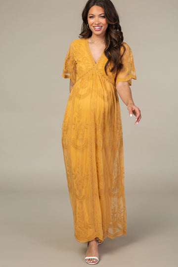 woman wearing a mustard yellow maternity maxi dress with short sleeves and floral lace detailing, showcasing her baby bump