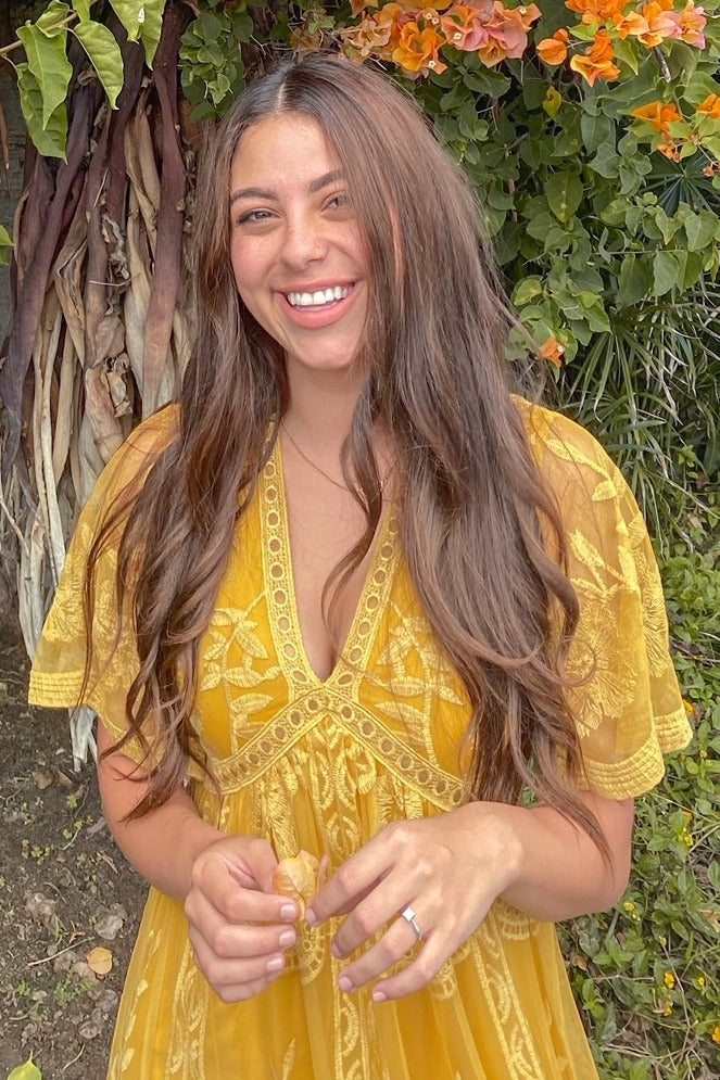 woman wearing a yellow embroidered short sleeve dress with a v-neckline and flowy silhouette, smiling outdoors