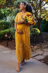 woman wearing a yellow maternity dress with floral details and holding a bouquet, showing her baby bump