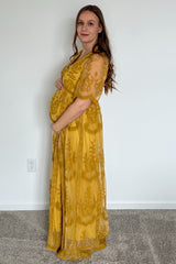 woman wearing a yellow maternity gown with floral embroidery, holding her baby bump