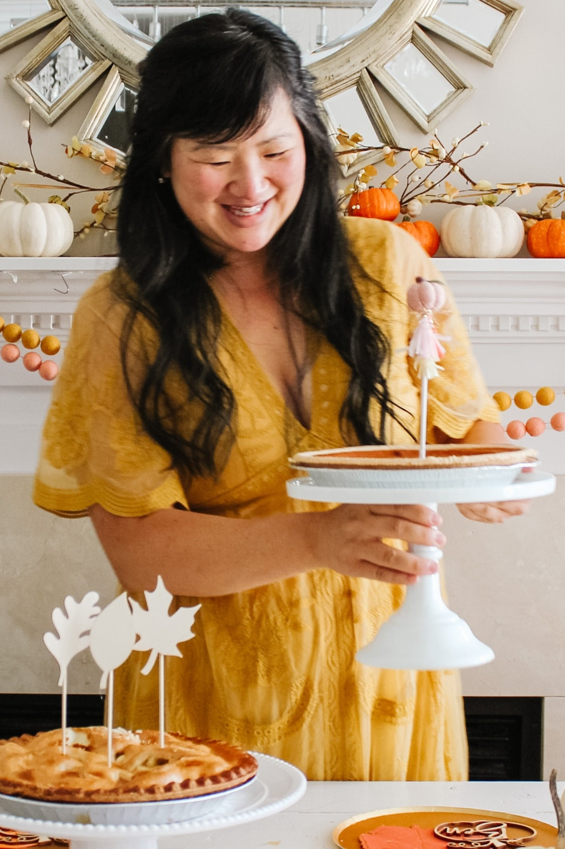 woman wearing a yellow lace dress holding a cake stand with pies on a table decorated for a celebration