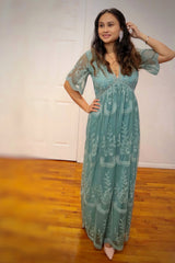 woman wearing a mint green maxi dress with floral embroidery and short sheer sleeves, standing with one hand raised