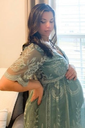 woman wearing a green embroidered maternity dress showcasing her baby bump