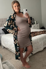 woman wearing a beige maternity dress with a floral kimono, showing her baby bump while posing in a bedroom