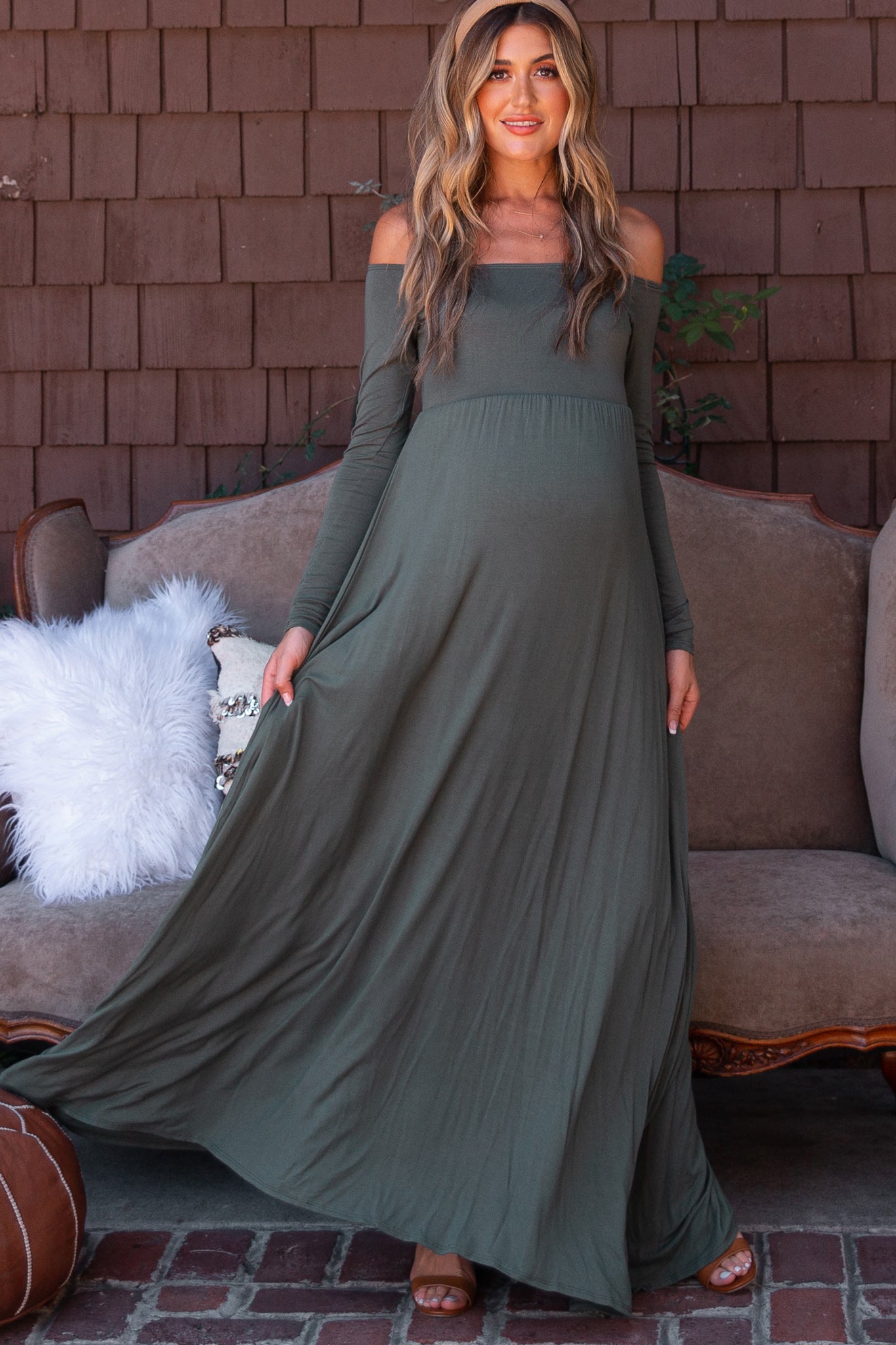 woman wearing an olive green off-shoulder maternity maxi dress with a flowing skirt and a visible baby bump