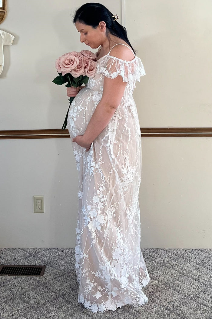 pregnant woman in white floral lace maternity dress holding a bouquet of pink roses